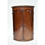 A Georgian inlaid mahogany bowfronted corner cupboard, the twin doors enclosing three fixed shelves,