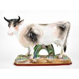A late 19th/early 20th century hand painted porcelain model cow on naturalistically modelled base