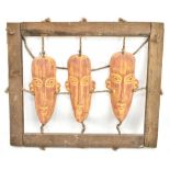A set of three African painted ceramic stylised busts suspended on rope and housed in wooden