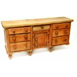 A Victorian pine dresser base comprising six drawers around a central cupboard on bottle feet,
