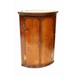 An oak cross banded two-door bow front wall-hanging corner cupboard, with brass H hinges,