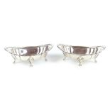 ATKIN BROS; a pair of Edwardian hallmarked silver oval dishes raised on four scrolling feet,