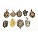 Eight silver shield shaped watch fobs, some with engraved detail, also a yellow metal example,