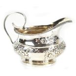 An embossed white metal cream jug with bead decorated rim, length 12.5cm, approx 4.2ozt/130.7g.