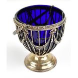 An Edwardian hallmarked silver swing handled bowl with damaged blue glass liner and swag motifs to