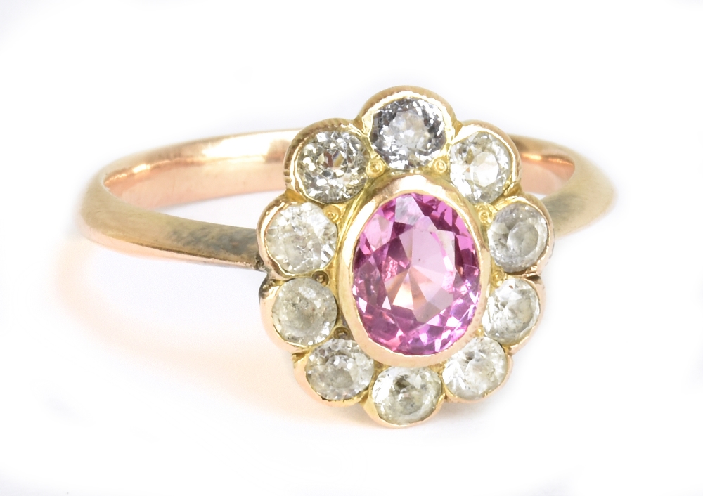 A 1920s yellow metal floral dress ring with outer border of clear stones and central oval pink