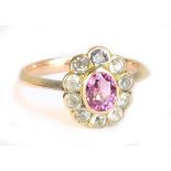 A 1920s yellow metal floral dress ring with outer border of clear stones and central oval pink