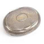 An Edward VII hallmarked silver tobacco box of oval form, with planished decoration surrounding an