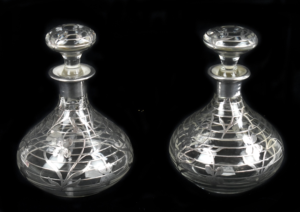 A pair of early/mid-20th century clear glass scent bottles and stoppers, with white metal overlay of