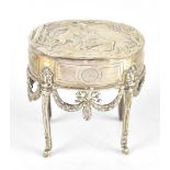 A Victorian hallmarked silver oval dressing table box on stand, with repoussé decoration depicting a