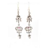 A pair of white metal filigree drop earrings set with diamonds and single red stone to each.
