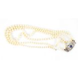 A cased three-strand pearl necklace with white metal clasp set with blue spinel and diamonds,