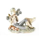 A Lladró figure of a young shepherd boy seated on a grassy knoll playing pan pipes,