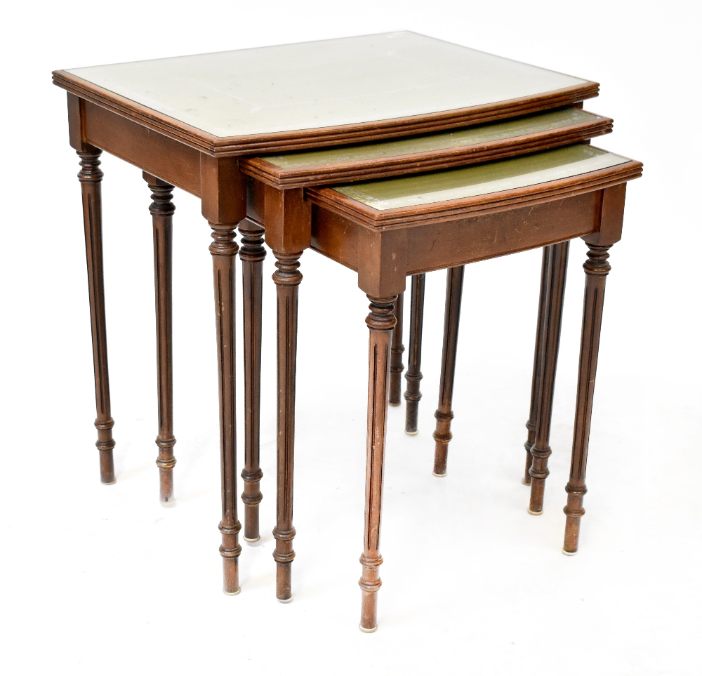 A nest of three reproduction mahogany tables with faux leather inserts and glass tops,
