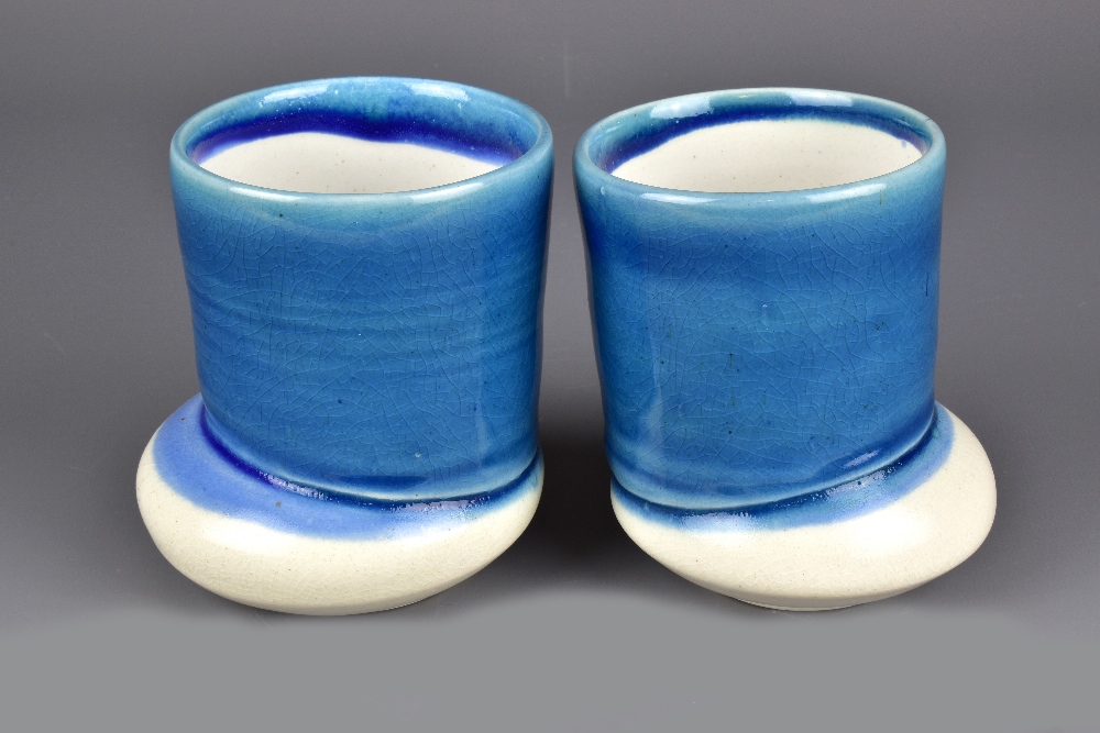 JENI HANSEN GARD; a pair of cups on off centre bases washed in blue glaze, tallest 10.5cm (2).