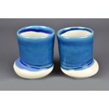 JENI HANSEN GARD; a pair of cups on off centre bases washed in blue glaze, tallest 10.5cm (2).