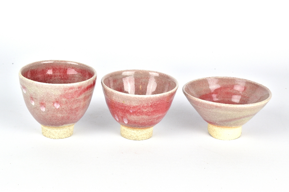 CLAYTON AMEMIYA; a group of three stoneware sake cups washed in copper red glaze, incised CA