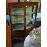 An Edwardian mahogany serpentine fronted display cabinet, the twin glazed doors enclosing fixed