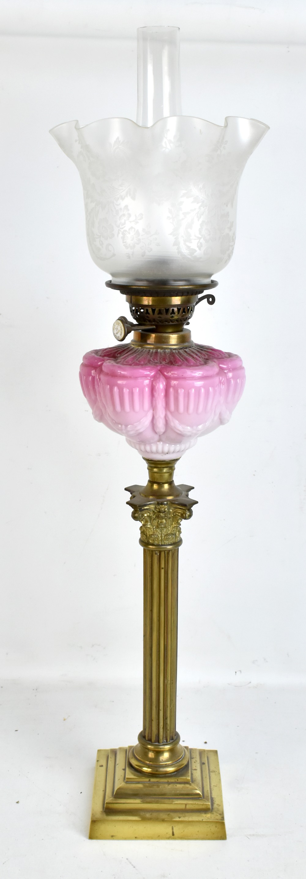 A Victorian brass Corinthian column oil lamp with pink glass reservoir featuring relief decoration