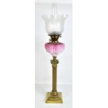 A Victorian brass Corinthian column oil lamp with pink glass reservoir featuring relief decoration