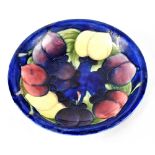 A Moorcroft Pottery shallow dish decorated with plums on a blue ground,