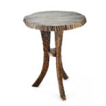 A small rustic locally hand-carved stool of simple form with shaped top above three outswept