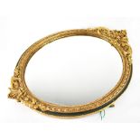 An 18th century style oval gilt-framed mirror surmounted by C-scrolls and foliate motifs within a