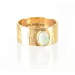 A 1970s 9ct gold contemporary ring of a textured band adorned with an oval white opal in gold bezel,