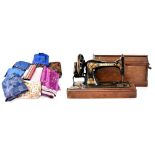A cased Singer sewing machine with painted decoration and a small quantity of various fabrics.
