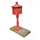 A painted red cast metal postbox on stand decorated with a horse and rider and bugles,