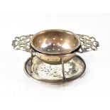 A George V hallmarked silver tea strainer on stand, circular with pierced foliate handles,