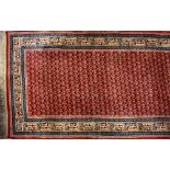 An Indian wool runner, central floral panel on a red ground within a multi-pattern border,