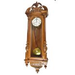 A late Victorian walnut Vienna style wall clock with arched pediment above two-piece white enamel