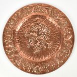 An Arts & Crafts copper charger with embossed decoration depicting a griffin inside a floral border,
