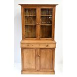 A pine side cabinet, the upper section with moulded cornice above two glazed doors enclosing two