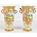 NORITAKE; a pair of hand painted twin handled pedestal vases decorated with roses and landscape