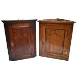 Two George III oak flat fronted hanging corner cupboards, one with oval inlaid detail to the door (