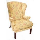 A Georgian-style wing armchair upholstered in a woven floral fabric, on square fluted legs.
