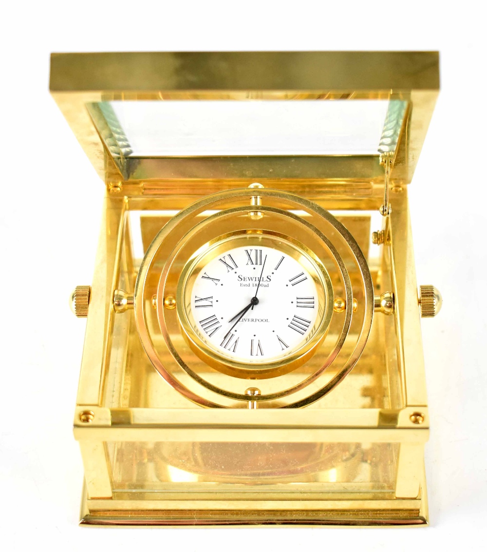 A boxed Sewills brass-cased gimbal mantel clock, the dial set with Roman numerals, 8 x 8cm.