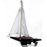 A black painted pond yacht with pale blue sails, deck adorned with a stuffed otter, length 97cm.