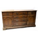 A Georgian-style oak dresser base of six drawers and two cupboard doors, on bracket feet,
