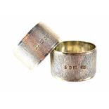 A pair of hallmarked silver napkin rings each with a wide textured band, in presentation boxes,