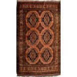 An early 20th century Middle Eastern wine ground rug with geometric pattern and fringed edge,