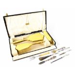 A cased three-piece yellow enamel vanity set and a quantity of hallmarked silver mounted utensils.