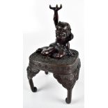 A Japanese Meiji period bronze figure of an Oni with arm raised aloft and seated on a table with