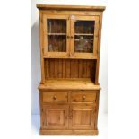 A reproduction pine side cabinet, the upper section with twin glazed doors above a recess and base