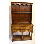 A small reproduction oak dresser, the upper section with boarded two shelf plate rack, the base with