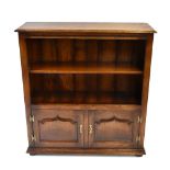 A reproduction oak open fronted bookcase with single fixed shelf above twin panelled cupboard doors,