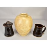 Leach Pottery; a stoneware jar and cover and a mug both covered in tenmoku breaking to kaki glaze,