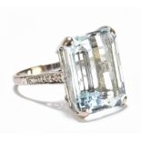 A white metal emerald cut aquamarine dress ring with small melee diamonds set to the shoulders,